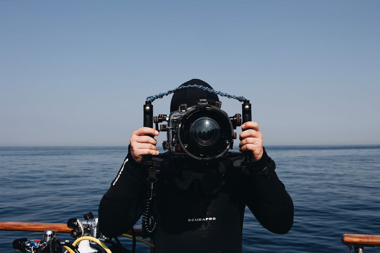 A scuba diver holding an underwater camera setup while on a boat by the sea.